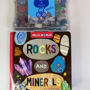 Może przedstawiać: Edukacyjny zestaw geologiczny z przezroczystym plastikowym pojemnikiem wypełnionym skałami i książką zatytułowaną "Rocks and Minerals" autorstwa Jill McDonald. Okładka książki zawiera kolorowe ilustracje skał i kryształów.