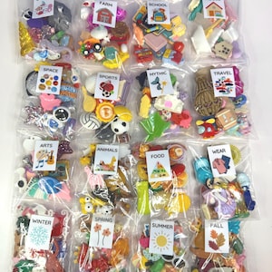 Peut inclure: Une collection de petits embellissements colorés dans des sacs en plastique transparents, chacun étiqueté avec un thème tel que "Océan", "Ferme", "École" et "Sports". Les sacs contiennent divers objets décoratifs de différentes formes et tailles.