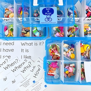 Peut inclure: Une boîte de rangement en plastique bleu avec plusieurs compartiments remplis de petits objets en plastique assortis dans des sachets transparents, étiquetés avec des sons phonétiques. Inclut des cartes imprimées avec des phrases.