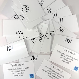 May include: A collection of white flashcards with black phonetic symbols and instructions for pronunciation. Some cards display symbols like /m/, /p/, and /k/. Other cards provide tips for saying sounds like /d/, /t/, and /g/.