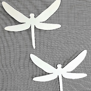 Puede incluir: Dos recortes de libélula de papel blanco sobre un fondo gris texturizado.