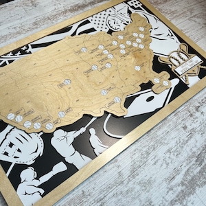 May include: A wooden baseball travel map of the United States, featuring baseball stadium locations marked with baseball icons. The map is set against a black and white background with baseball-themed graphics and text that reads "Calease Family Baseball Travel Map."