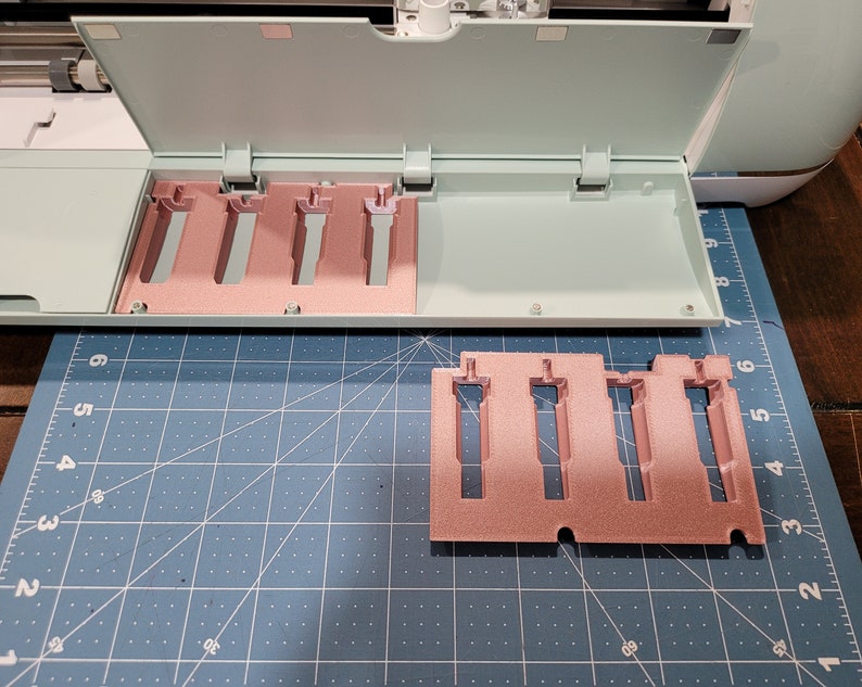Pode incluir: Um porta-ferramentas de pl&aacute;stico de cor verde claro e rosa com cinco ranhuras para guardar ferramentas. O porta-ferramentas est&aacute; aberto e as ranhuras est&atilde;o vazias. O porta-ferramentas est&aacute; sobre um tapete de corte azul.