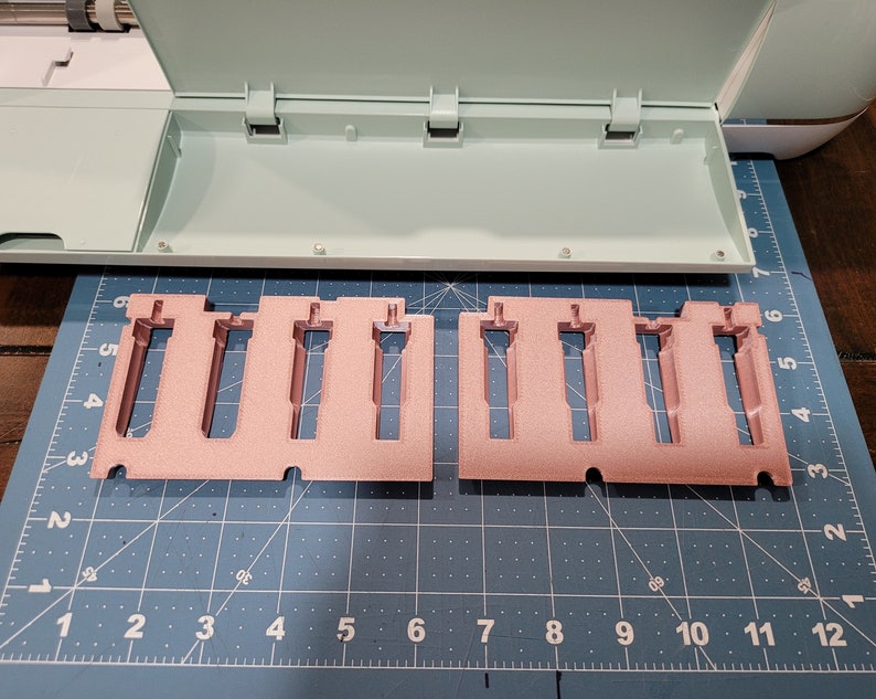 Pode incluir: Dois porta-ferramentas de pl&aacute;stico rosa com ranhuras para segurar ferramentas. Os suportes est&atilde;o sobre uma superf&iacute;cie de grade azul e branca.