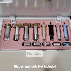 May include: A close-up of a set of 8 different coloured cutting blades and tools for a crafting machine. The blades are arranged in a row in a white and pink case. The text "Rose Gold" is visible on the case. The text "Blades and tools Not Included" is visible below the case.