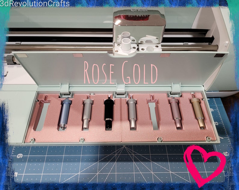 Pode incluir: Ferramentas de corte Cricut cor ouro rosa em uma caixa de armazenamento. As ferramentas est&atilde;o dispostas em uma fila e todas s&atilde;o do mesmo tamanho. A caixa est&aacute; aberta e as ferramentas s&atilde;o vis&iacute;veis. A caixa &eacute; feita de pl&aacute;stico azul claro e tem um interior rosa.