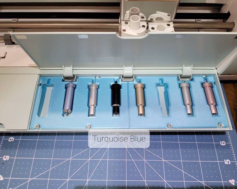 Pode incluir: Close-up de um conjunto de sete l&acirc;minas de corte de diferentes cores para uma m&aacute;quina de corte artesanal. As l&acirc;minas est&atilde;o dispostas em uma fila em um suporte de espuma azul. O texto "Turquoise Blue" &eacute; vis&iacute;vel abaixo das l&acirc;minas.