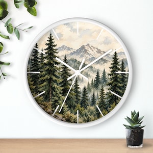 May include: A round wall clock with a white frame featuring a watercolor-style print of a dense pine forest and snow-capped mountains in the background. The clock face has simple white hour and minute hands against the detailed landscape scene.