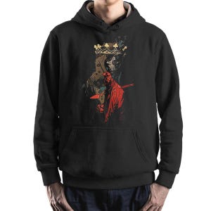 May include: Black hooded sweatshirt featuring a graphic print of a red character with a crown and a skull. The character is holding a sword.