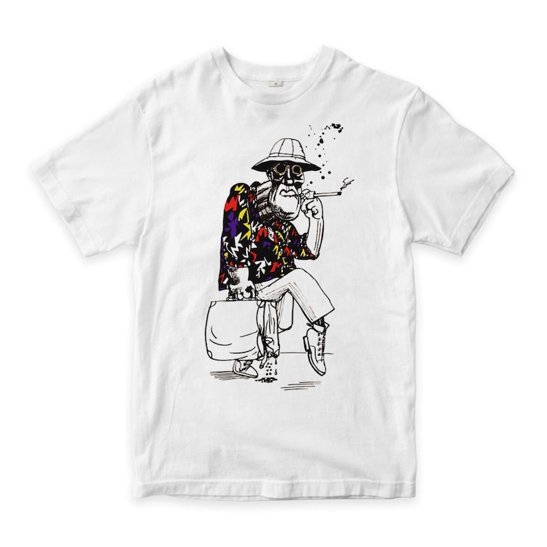 May include: White t-shirt with a black and white illustration of a seated figure wearing a hat and smoking. The figure is dressed in a colourful floral shirt, white trousers, and boots, holding a suitcase. Black ink splatters are above the figure.