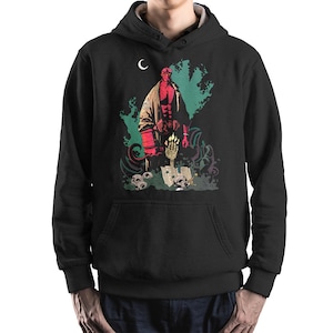 May include: Black hooded sweatshirt with a graphic print of a red-skinned character holding a large gun, standing in front of a skull and a book. The character is surrounded by a green and black background with a crescent moon in the top left corner.