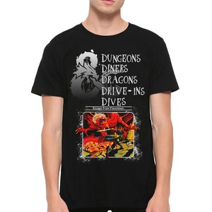 May include: Black t-shirt featuring a graphic with the text "DUNGEONS DINERS DRAGONS DRIVE-INS DIVES" and a dragon illustration. The graphic also includes the phrase "Escape From Flavortown."