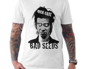 May include: White t-shirt featuring a black and white graphic of Nick Cave with the text "NICK CAVE" above his head and "AND THE BAD SEEDS" below. The design is a bold, stylized portrait.