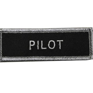 May include: A black embroidered patch with a white border and the word "PILOT" in white lettering.