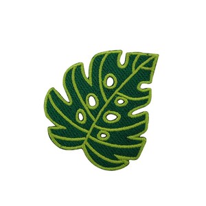 May include: A green embroidered patch in the shape of a monstera leaf. The leaf has a dark green fill with lighter green outlining and details. The leaf features several oval-shaped cutouts.