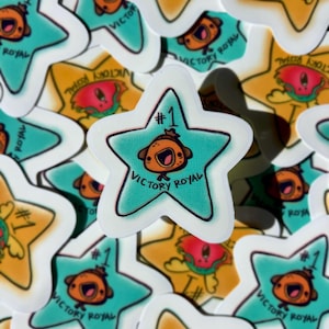 May include: A collection of star-shaped stickers with a cartoon character and the text "Victory Royal." The stickers feature a teal star with a cartoon character, the number "1," and the words "Victory Royal." Other stickers have a yellow star with a similar design.