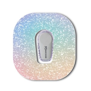 May include: A Dexcom G6 continuous glucose monitor transmitter centered on a square adhesive patch with rounded corners. The patch features a glittery, iridescent gradient pattern transitioning from light blue at the top to soft pink at the bottom.