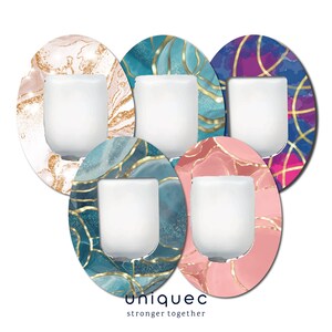 Peut inclure: Cinq bougeoirs décoratifs avec des motifs abstraits. Chaque bougeoir contient une bougie blanche. Les motifs comprennent des accents de marbre et d'or dans des tons de rose, de bleu et de violet. Le texte "uniqueq" et "stronger together" est en bas.
