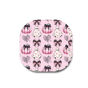 May include: A square-shaped patch with rounded corners featuring a repeating pattern on a light pink background. The design includes pink pumpkins with black polka dots, white ghosts with pink flower accents, black spiderwebs, and black bows with white dots.