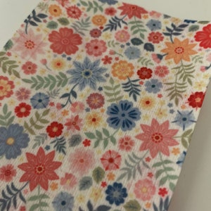 May include: A white fabric with a floral pattern featuring pink, red, blue, and yellow flowers. The fabric has a textured surface.