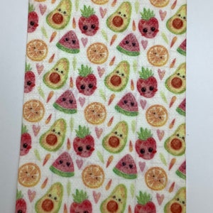 May include: White fabric with a repeating pattern of cartoon avocados, watermelons, strawberries, and orange slices. The fruit has smiling faces and hearts are scattered throughout the pattern.