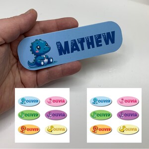 May include: A set of colorful oval-shaped iron-on labels with a dinosaur design. The labels feature the names "Oliver" and "Olivia". There is also a blue label with the name "Mathew" on it.