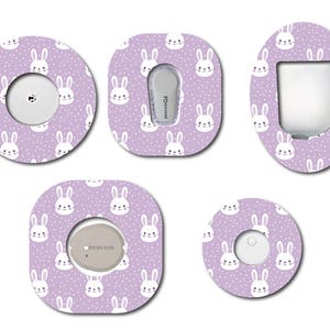 May include: Five different sized adhesive bandages with a purple background and a white bunny rabbit pattern. The bandages are designed to cover medical devices.
