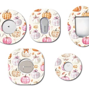 May include: A collection of decorative adhesive patches featuring a fall-themed pumpkin pattern. The patches are in various shapes and sizes, with a cream background and watercolor pumpkins in shades of orange, pink, and white. Some patches have openings for medical devices.