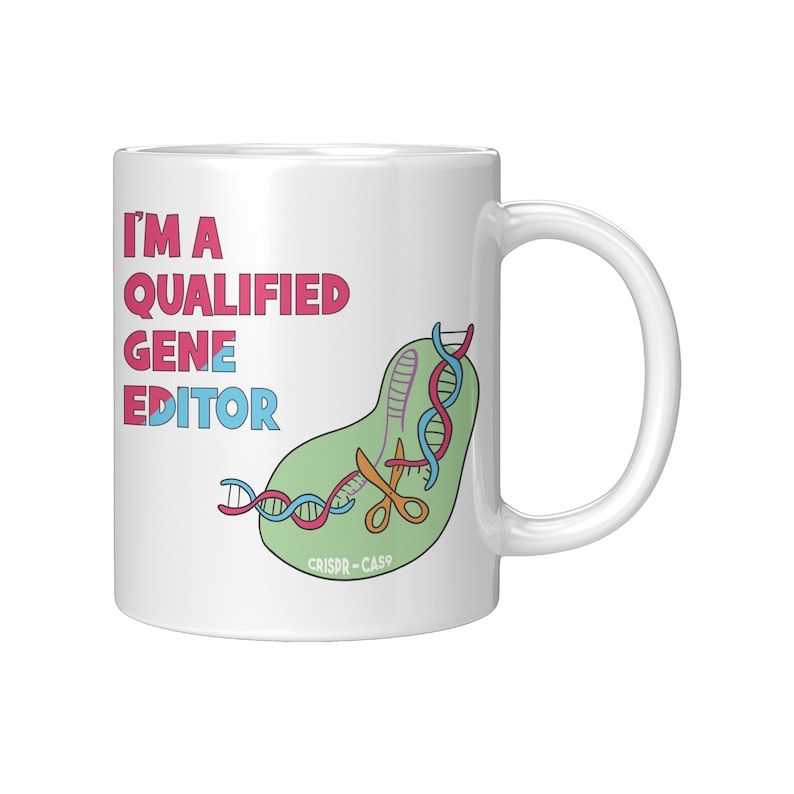 Peut inclure: Une tasse en c&eacute;ramique blanche avec une illustration verte, rose et bleue d'une cha&icirc;ne d'ADN coup&eacute;e par des ciseaux. Le texte "I'm a Qualified Gene Editor" est imprim&eacute; en rose et bleu sur la tasse. Le texte "CRISPR-CAS9" est imprim&eacute; en noir sous l'illustration.