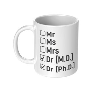 Puede incluir: Taza de café de cerámica blanca con una lista de verificación de títulos, que incluyen "Mr", "Ms", "Mrs", "Dr [M.D.]" y "Dr [Ph.D.]". Los dos últimos títulos están marcados.