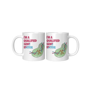 Peut inclure: Deux tasses en c&eacute;ramique blanche avec une illustration verte, bleue et rose d'une cha&icirc;ne d'ADN coup&eacute;e par des ciseaux. Le texte "Je suis un &eacute;diteur de g&egrave;nes qualifi&eacute;" est imprim&eacute; sur chaque tasse.