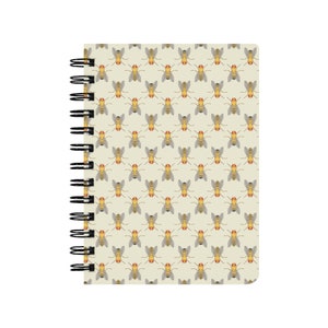 以下が含まれることがあります： 薄いベージュの表紙に、黄色と灰色のハエが繰り返し描かれた、スパイラルバインディングのノートブックです。