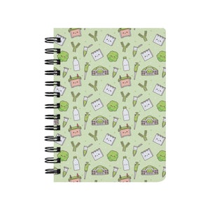 May include: A spiral-bound notebook with a pale green cover. The cover has a repeating pattern of cartoon science illustrations, including flasks and beakers. The notebook has a black spiral binding. The measurements are in cm.