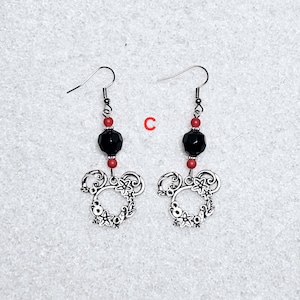 K&ouml;nnte beinhalten: Ein Paar silberne Ohrringe mit einer schwarzen facettierten Perle und roten Perlen. Die Ohrringe haben ein silbernes Mickey-Maus-Kopfdesign.