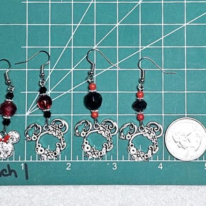 K&ouml;nnte beinhalten: Drei Paar silberne Ohrringe mit roten und schwarzen Perlen. Jeder Ohrring hat einen silbernen Anh&auml;nger in Form eines Mickey-Mouse-Kopfes.