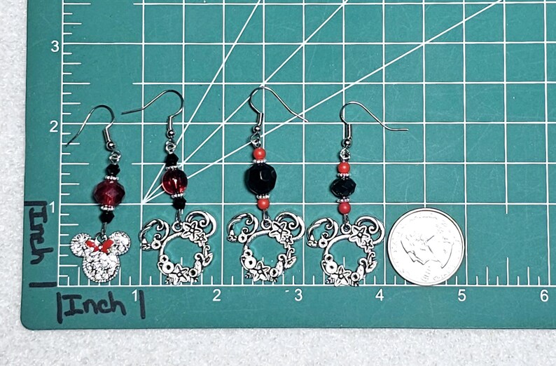 K&ouml;nnte beinhalten: Drei Paar silberne Ohrringe mit roten und schwarzen Perlen. Jeder Ohrring hat einen silbernen Anh&auml;nger in Form eines Mickey-Mouse-Kopfes.