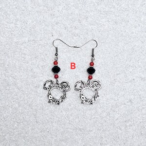 K&ouml;nnte beinhalten: Ein Paar silberne Ohrringe mit einem floralen Design in Form von Mickey Mouse. Die Ohrringe haben rote und schwarze Perlen.
