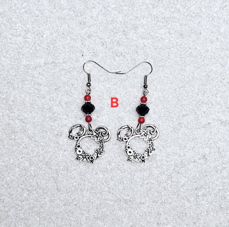 K&ouml;nnte beinhalten: Ein Paar silberne Ohrringe mit einem floralen Design in Form von Mickey Mouse. Die Ohrringe haben rote und schwarze Perlen.
