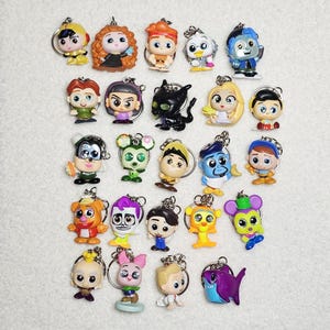 May include: A collection of colorful character keychains, each with a silver keyring. The keychains feature various cartoon characters in different poses and outfits. The keychains are made of plastic and are on a white background.