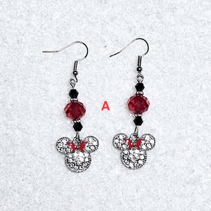 K&ouml;nnte beinhalten: Ein Paar silberne Ohrh&auml;nger mit einer roten und schwarzen Kristallperle und einem silbernen Minnie Mouse-Anh&auml;nger mit Strasssteinen.