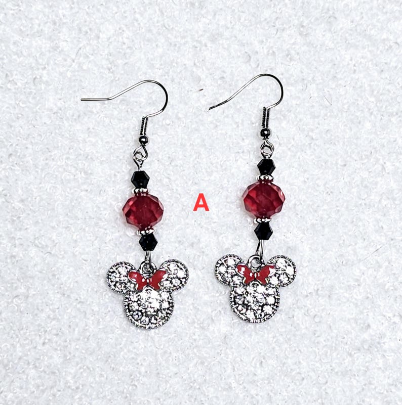 K&ouml;nnte beinhalten: Ein Paar silberne Ohrh&auml;nger mit einer roten und schwarzen Kristallperle und einem silbernen Minnie Mouse-Anh&auml;nger mit Strasssteinen.