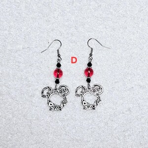 K&ouml;nnte beinhalten: Ein Paar silberne Ohrringe mit einem floralen Design und einer roten Glasperle. Die Ohrringe h&auml;ngen an silbernen Haken.
