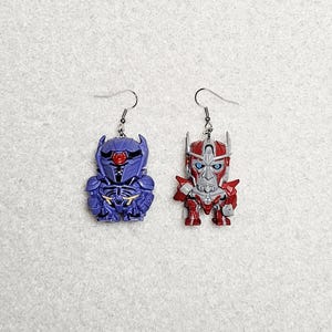 May include: A pair of novelty earrings featuring robot character designs. One earring is purple with gold accents, the other is red and silver. Both have silver-colored ear wires.