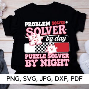 May include: Black t-shirt with pink text that reads "Problem Solver* Solver by day Puzzle Solver By Night". The text is surrounded by a pink puzzle piece with a smiling face.