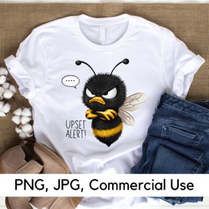 May include: White t-shirt featuring a cartoon image of an angry bee with black and yellow stripes. The bee has its arms crossed and a speech bubble above its head that says "Upset Alert!"