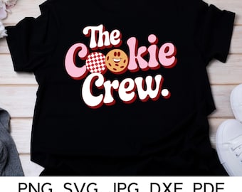May include: Black t-shirt with the text "The Cookie Crew" in pink and red letters. A red and white checkered cookie and a brown cookie with a smiley face are included in the design.