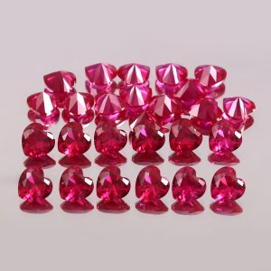 Peut inclure: Une collection de pierres précieuses rubis en forme de cœur, disposées en rangées, avec une surface réfléchissante montrant les pierres par le dessous.