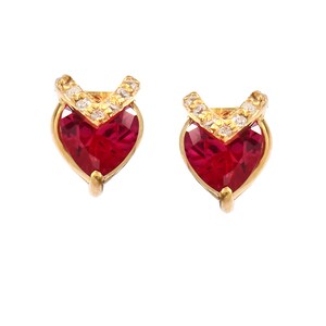 Puede incluir: Un par de pendientes de corazón de oro con piedras preciosas rojas y una fila de pequeñas piedras preciosas blancas alrededor de la parte superior de cada corazón.