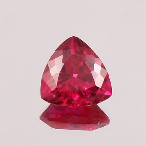 May include: A vibrant red triangular gemstone with a faceted cut. The gemstone is reflecting light, showcasing its brilliance.