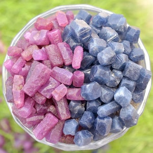 Op de afbeelding: Een glazen kom gevuld met ruwe edelstenen. De kom is verdeeld in twee secties, één met dieproze en magenta stenen, de andere met donkerblauwe stenen. De edelstenen hebben een ruwe, natuurlijke textuur.